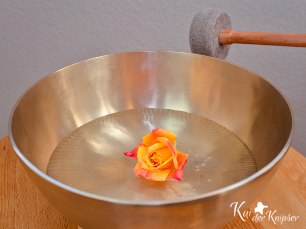 Klangschale mit gelber Rose und Klöppel, auf Holztisch. Fotografiert von Kai der Knipser. Ideal für Entspannung und Meditation.